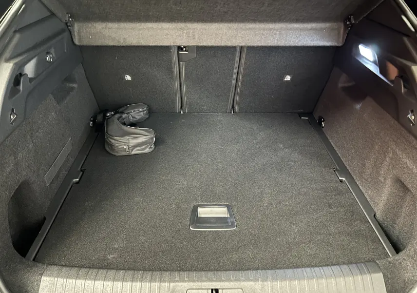 Vue intérieure du coffre spacieux et propre du Peugeot 3008 III Hybrid 145 e-DCS6 GT, avec un sac noir posé à gauche.