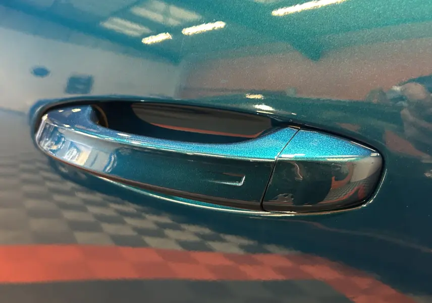 Poignée de porte côté gauche en gros plan sur Peugeot 3008 III Hybrid 145 bleu obsession avec finition brillante.