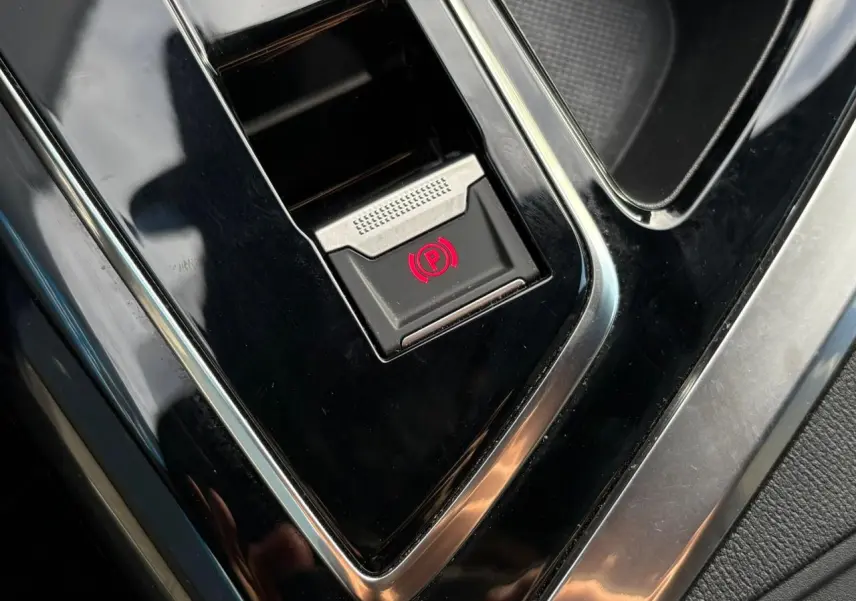 Gros plan sur le bouton de frein de stationnement électrique rouge dans la console centrale du Peugeot 3008 GT 2023.