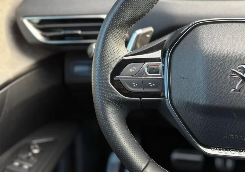 Gros plan sur le volant cuir perforé noir du Peugeot 3008 2023 avec commandes intégrées côté gauche et logo lion chromé.