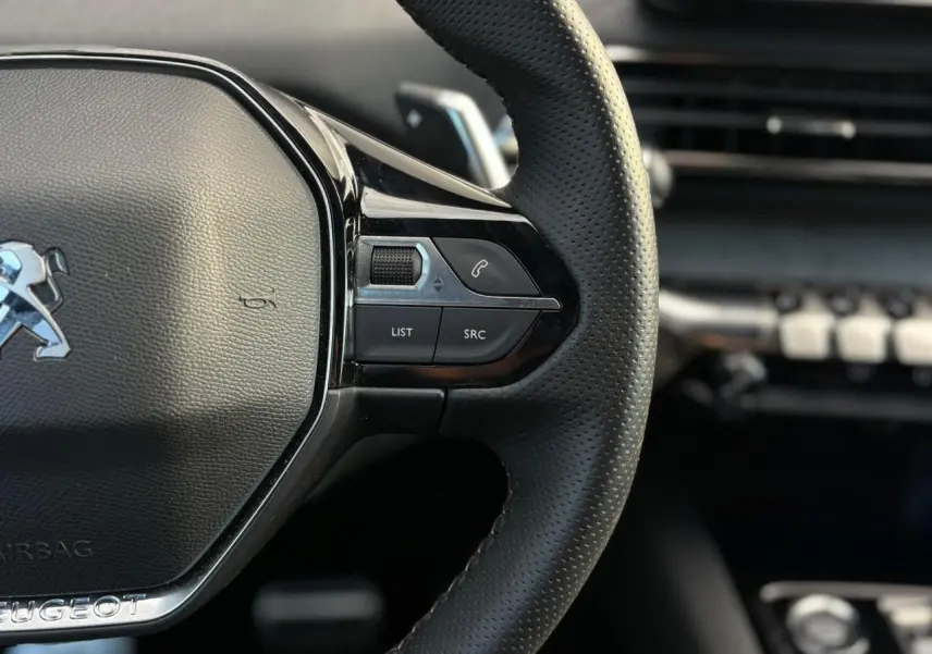 Gros plan sur le côté droit du volant cuir perforé du Peugeot 3008 GT 2023 avec commandes intégrées et finition noire brillante.