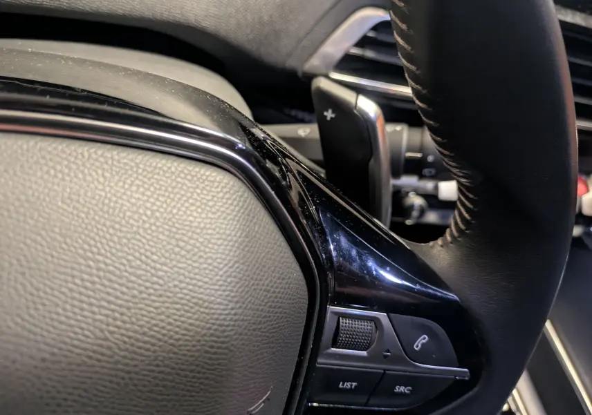 Gros plan sur la partie gauche du volant cuir noir du Peugeot 5008 2024, avec commandes intégrées et palettes au volant.