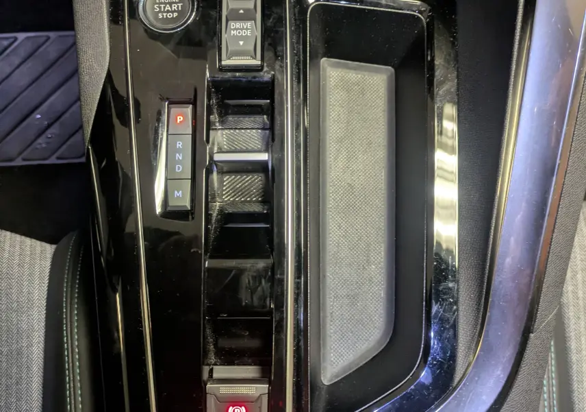 Gros plan sur la console centrale noire brillante du Peugeot 5008 2024 avec sélecteur de boîte auto et bouton start/stop.