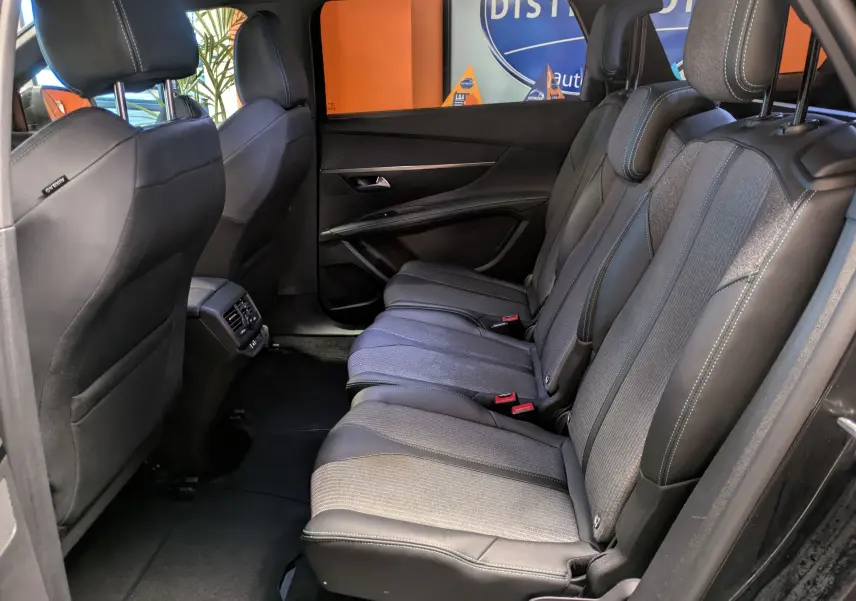 Vue intérieure côté droit des sièges arrière en sellerie TEP et tissu gris du Peugeot 5008 noir 2024, avec accoudoirs et aérateurs centraux.