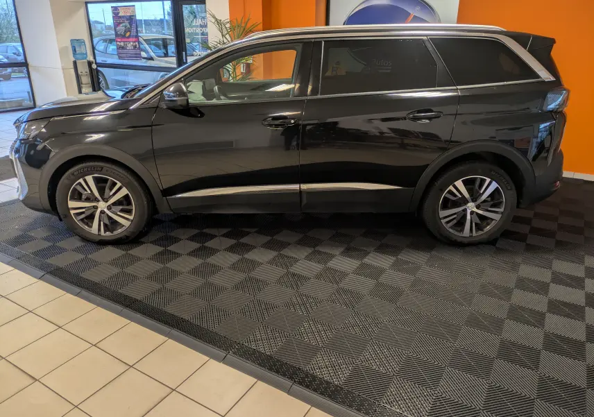 Vue de profil côté gauche d'un Peugeot 5008 noir 2024 en showroom, avec jantes aluminium 18 pouces et vitres surteintées.