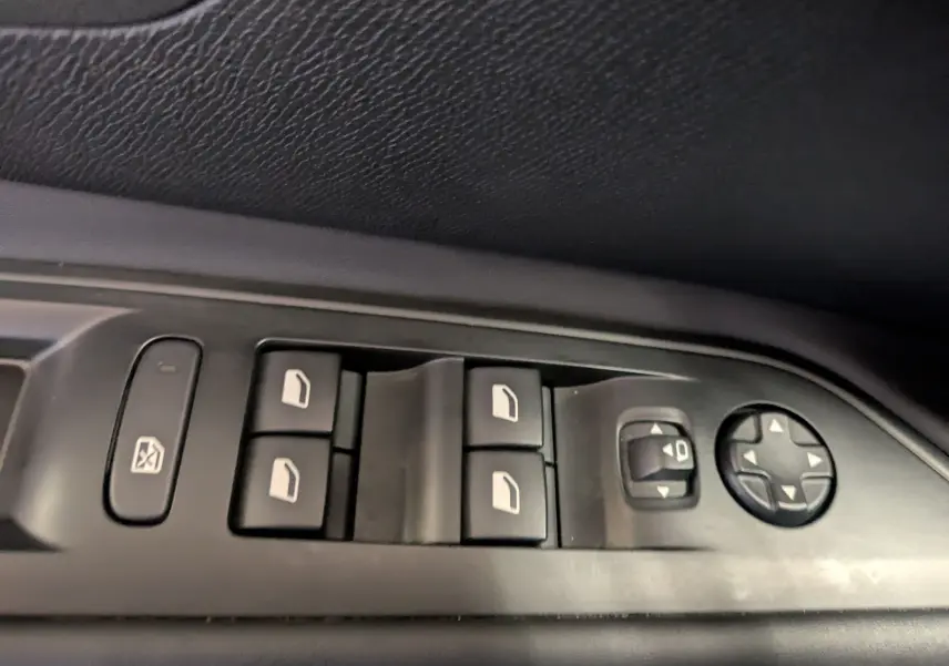 Gros plan sur les commandes de lève-vitres et réglage des rétroviseurs côté conducteur d’un Peugeot 5008 noir 2024.