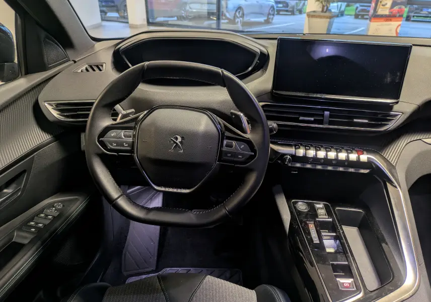 Vue intérieure centrée sur le volant cuir et tableau de bord du Peugeot 5008 2024, avec écran tactile et commandes modernes.