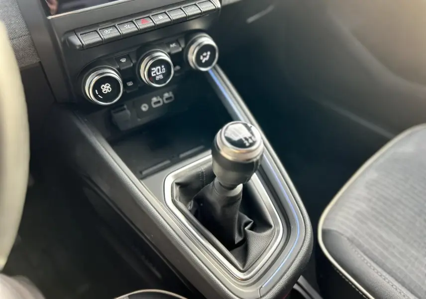 Gros plan sur la console centrale d’une Renault Clio 2025, boîte manuelle avec commandes de climatisation et sièges gris.