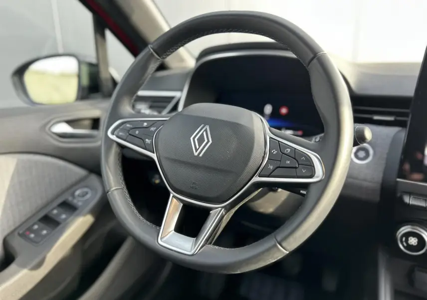 Gros plan sur le volant multifonction noir de la Renault Clio 2025, avec commandes intégrées et tableau de bord flou en arrière-plan.