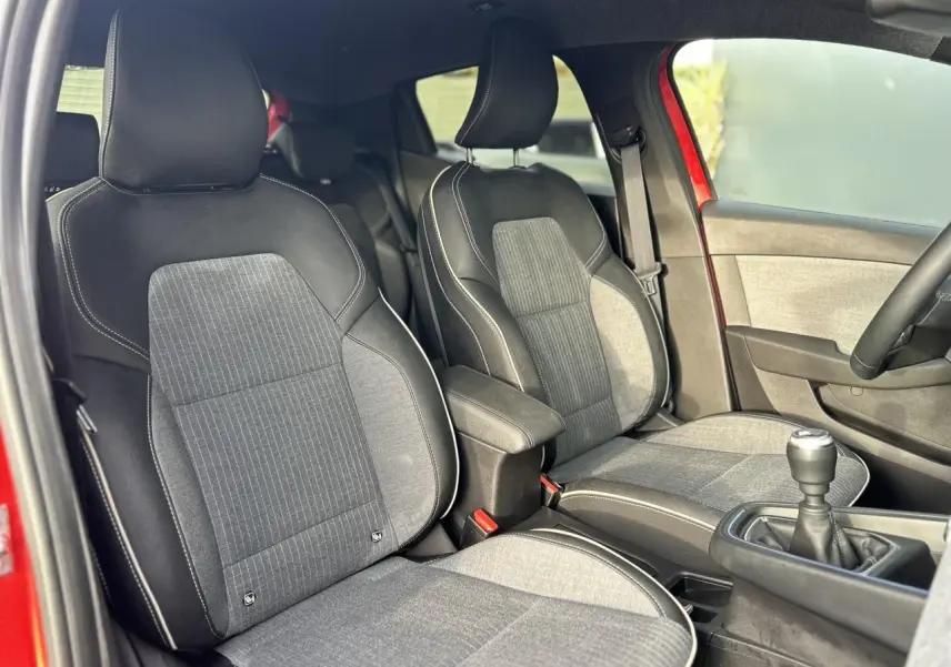 Vue intérieure côté avant gauche montrant les sièges tissu et cuir gris avec surpiqûres blanches d'une Renault Clio Rouge Désir.