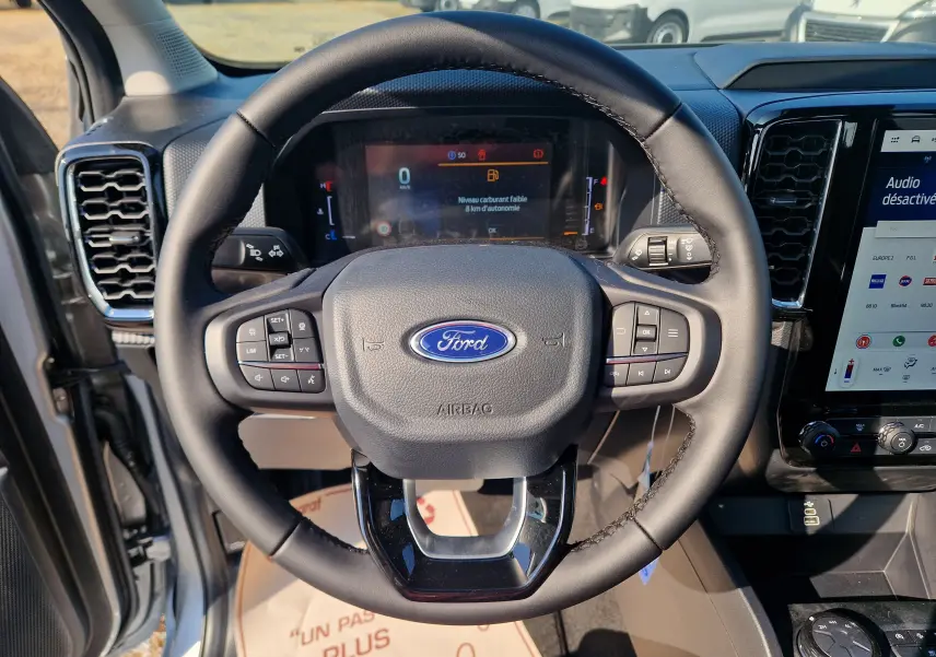 Vue rapprochée du volant noir du Ford Ranger Super Cabine 2026 gris, avec commandes intégrées et tableau de bord digital.
