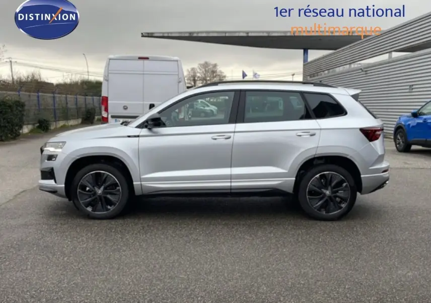 Vue latérale droite d’un Skoda Karoq gris argent métallisé 2025 avec jantes noires et toit blanc.