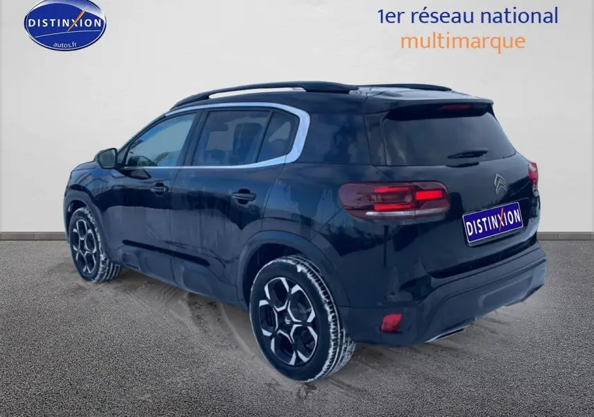 Vue 3/4 arrière droite d’un Citroën C5 Aircross noir 2025 avec jantes alu et barres de toit visibles.