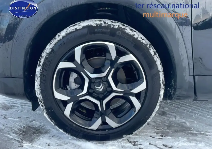 Gros plan sur la roue avant droite noire avec jante alu bicolore du Citroën C5 Aircross noir sous la neige.