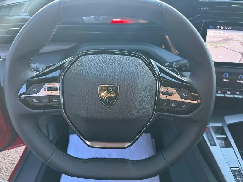 Vue rapprochée du volant multifonction noir avec logo Peugeot sur une 308 SW Rouge Elixir 2024, intérieur moderne visible.