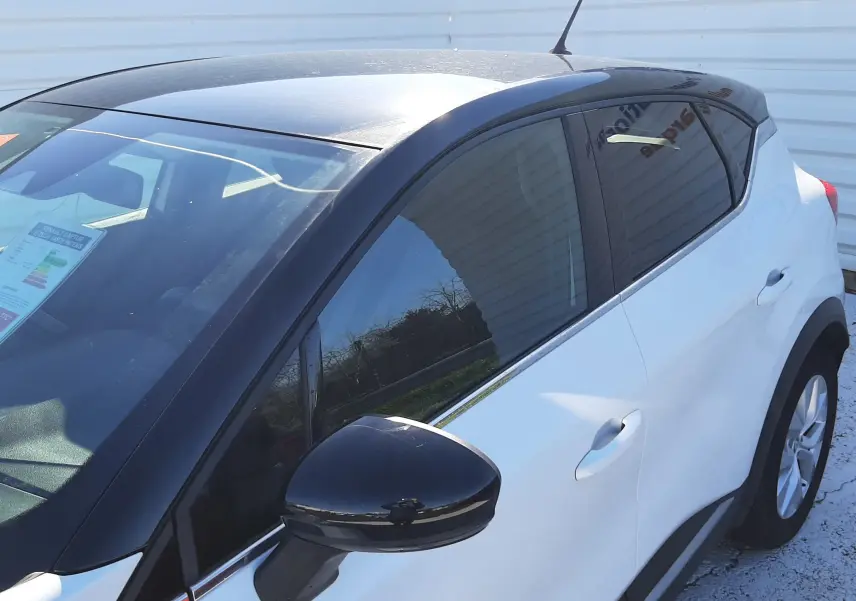 Vue côté gauche en 3/4 arrière d’un Renault Captur E-Tech blanc nacré avec toit et rétroviseur noir, vitres teintées.