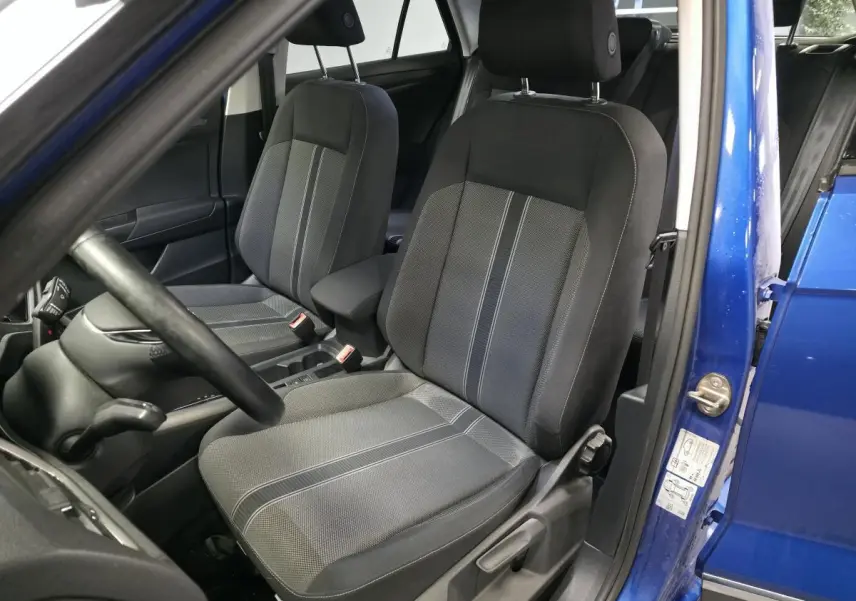 Vue intérieure côté conducteur du Volkswagen T-Roc bleu foncé, mettant en valeur les sièges avant en tissu gris avec accoudoir central.