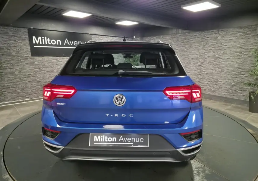 Vue arrière d'un Volkswagen T-Roc bleu foncé avec feux LED allumés dans un showroom intérieur.