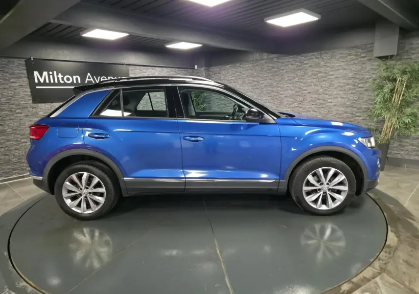 Vue de profil côté gauche d'un Volkswagen T-Roc bleu foncé avec jantes alliage 17 pouces dans un showroom.