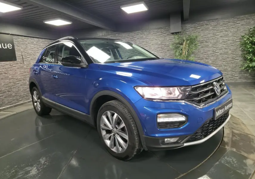Volkswagen T-Roc bleu foncé en 3/4 avant droit, avec jantes alliage et calandre chromée visible.