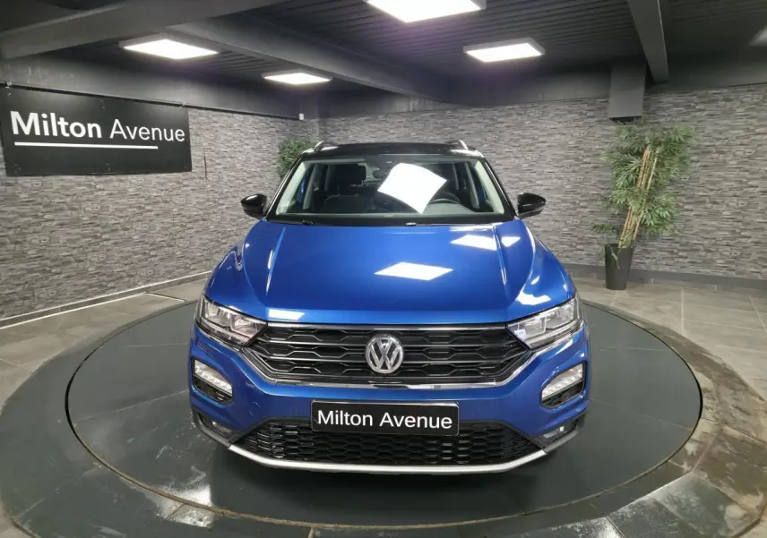 Vue avant d'un Volkswagen T-Roc bleu foncé avec calandre noire et toit noir dans un showroom.
