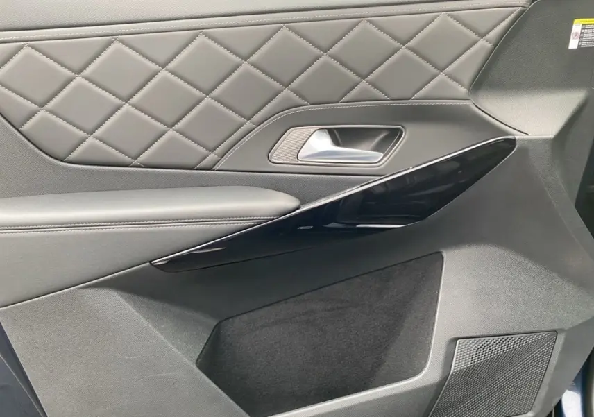 Gros plan sur la porte intérieure côté droit du DS7 Crossback 2024, avec cuir matelassé gris et insert noir brillant.