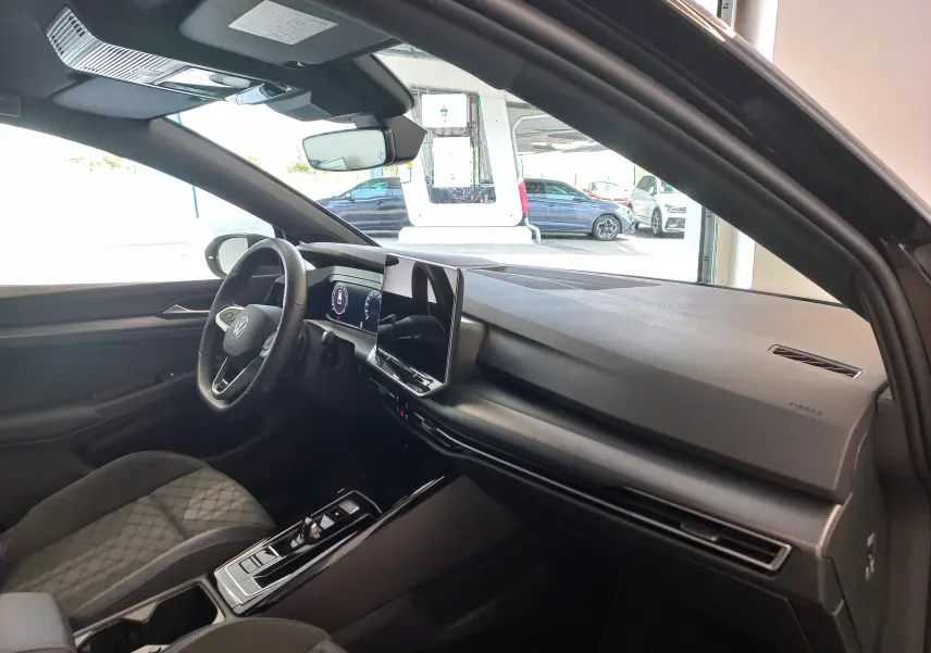 Vue intérieure côté conducteur de la Volkswagen Golf 1.5 eTSI 2025 noire, avec tableau de bord moderne et écran tactile central.