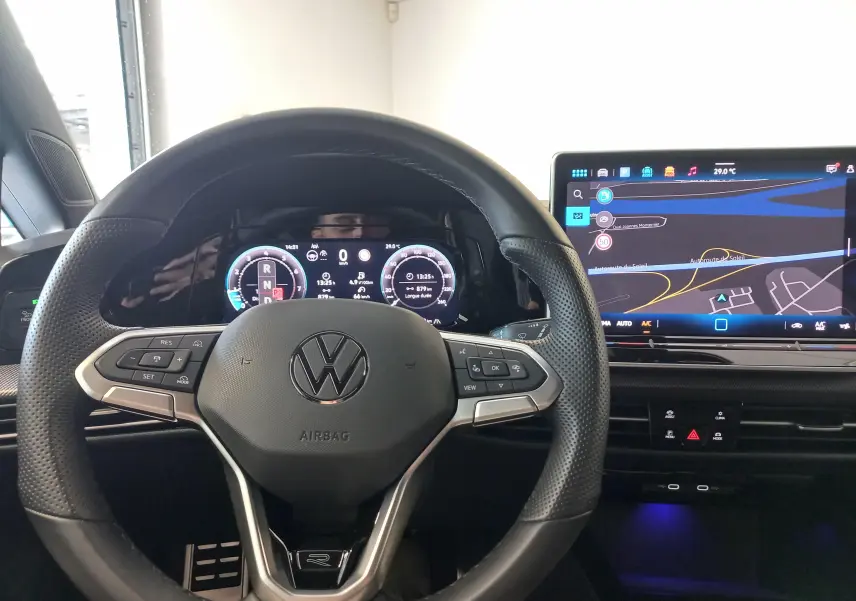 Vue intérieure centrée sur le volant noir perforé et l'écran numérique affichant la navigation de la Volkswagen Golf 1.5 eTSI R-Line.