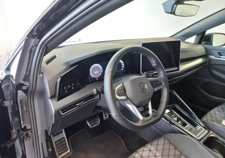 Vue intérieure côté conducteur de la Volkswagen Golf 1.5 eTSI R-Line 2025 noire, avec tableau de bord numérique et écran tactile.