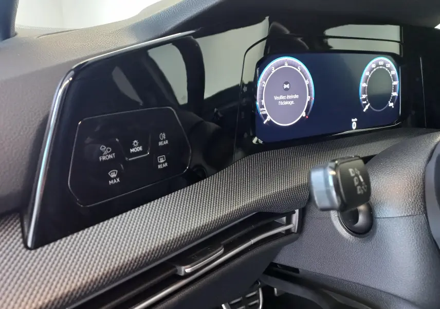 Vue rapprochée du tableau de bord numérique et des commandes d’éclairage du Volkswagen Golf 1.5 eTSI noir Ébène 2025.