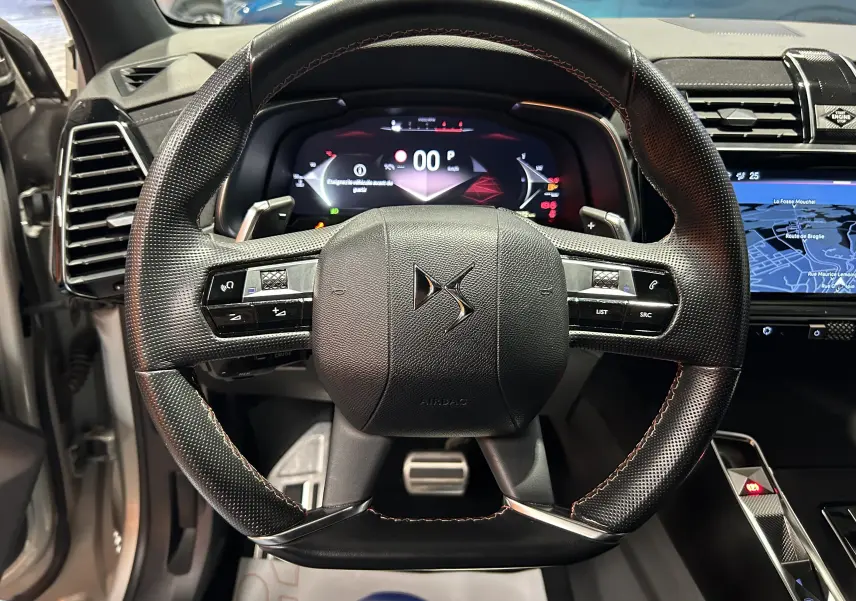 Vue centrée sur le volant en cuir noir avec surpiqûres rouges du DS7 2024, tableau de bord numérique et écran GPS visibles.