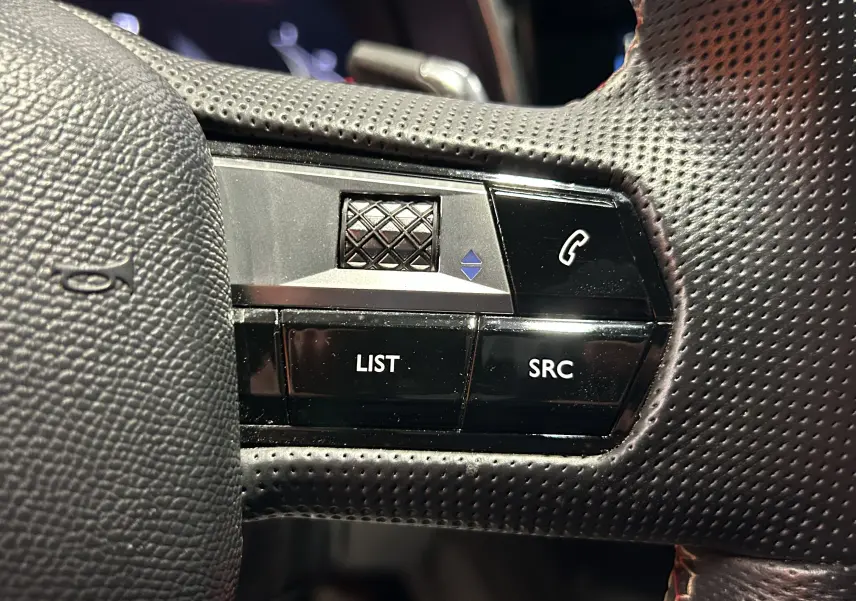 Gros plan sur les commandes noires du volant perforé côté gauche du DS7 BlueHDi 130 2024, boutons LIST et SRC visibles.