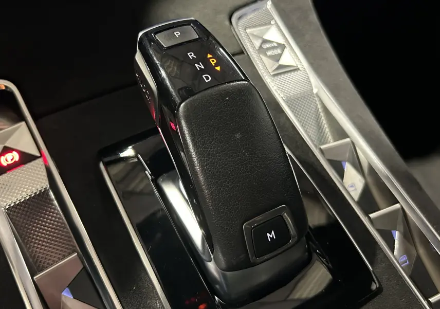 Le levier de vitesses automatique noir en cuir du DS7 2024, avec boutons de commande et éclairage ambiant visible.