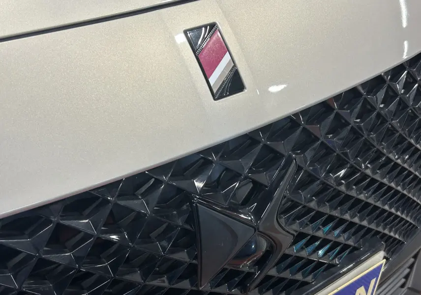 Gros plan sur la calandre noire texturée et l'emblème DS sur la face avant d'une DS7 Cristal Pearl 2024.