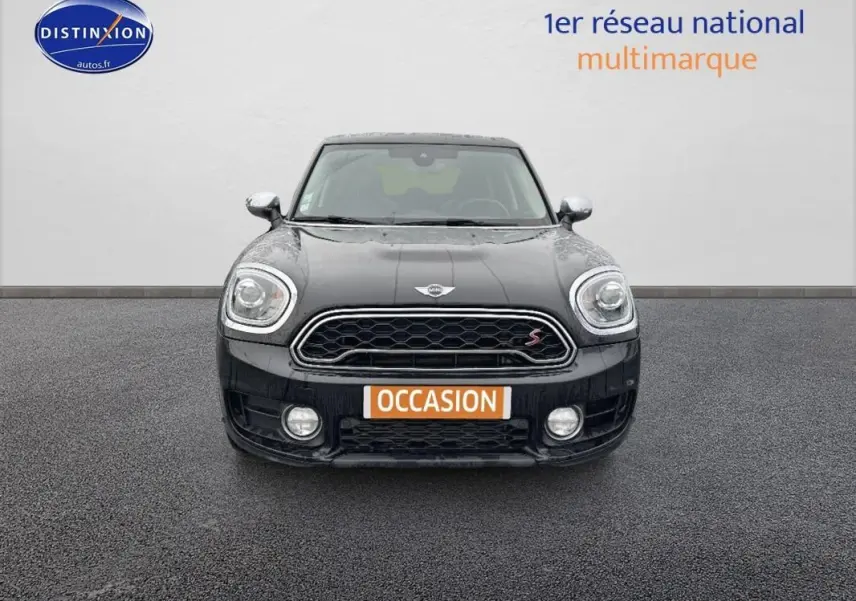 Vue frontale d'une MINI Countryman noire avec calandre hexagonale et feux avant allumés sur fond neutre.