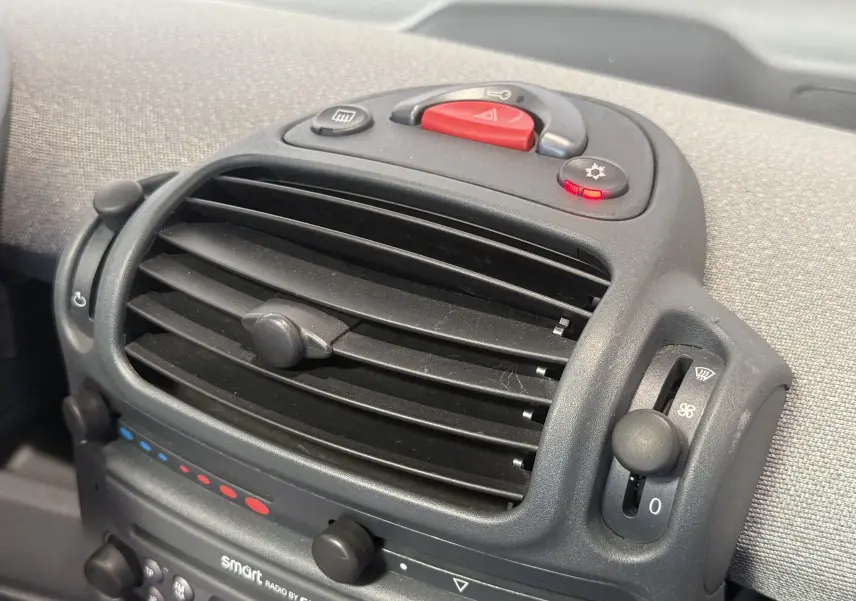 Gros plan sur la console centrale noire avec commandes de ventilation et bouton d'alerte de la Smart Fortwo beige 2004.
