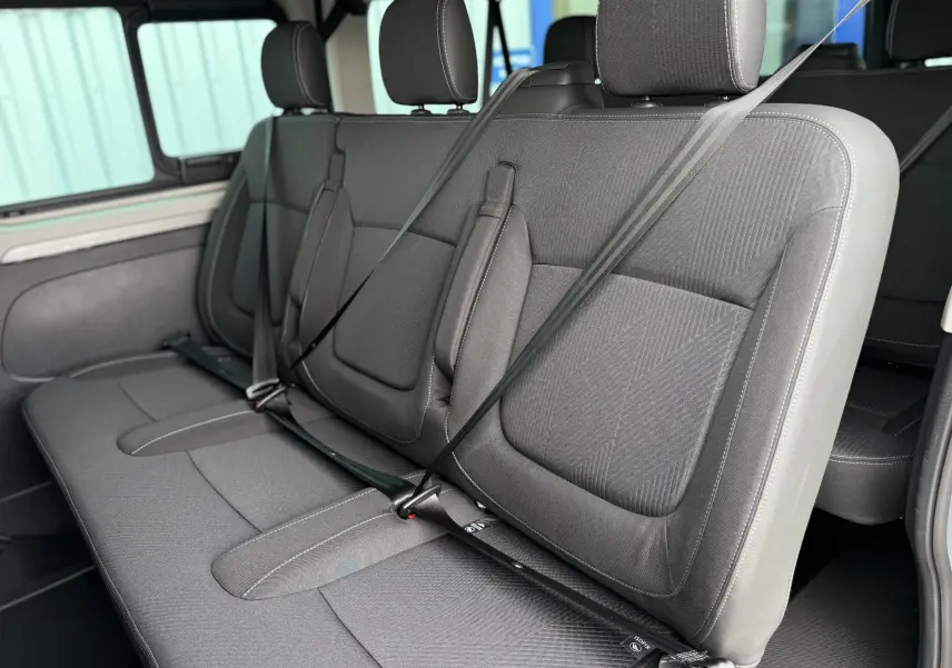 Vue intérieure sur les sièges arrière gris tissu du Renault Trafic Combi L2 2025, avec ceintures de sécurité attachées.