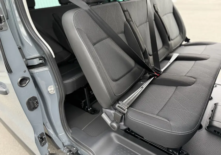 Vue intérieure côté gauche des sièges arrière en tissu gris du Renault Trafic Combi L2 2025 avec porte ouverte.