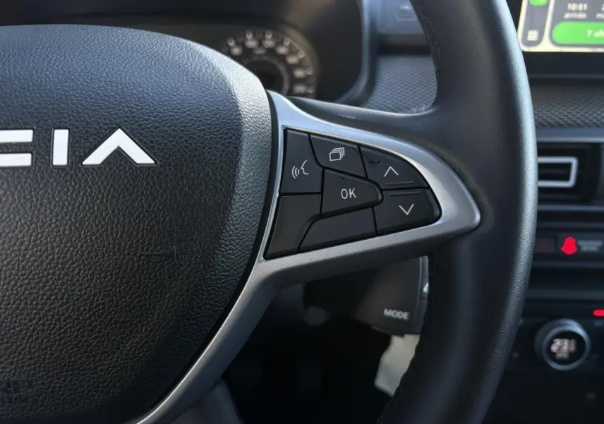 Gros plan sur le volant noir du Dacia Jogger 2025, avec commandes multifonctions et partie centrale en relief.
