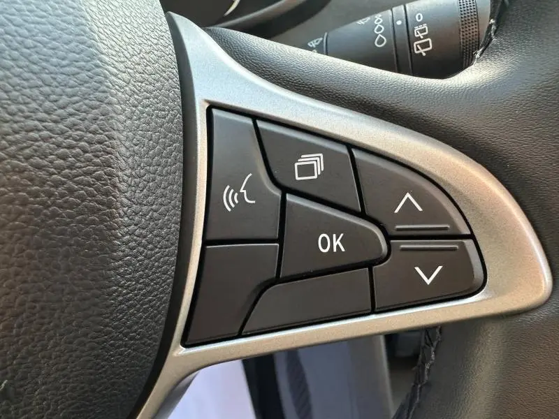 Gros plan sur les commandes multifonctions à droite du volant du Dacia Sandero blanc Glacier 2025, boutons noirs avec cadre argenté.