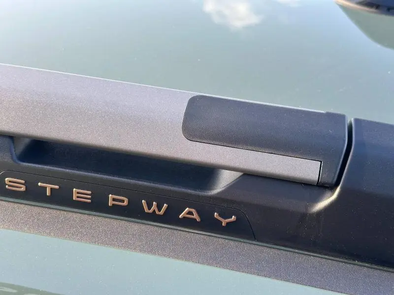 Gros plan sur la poignée de coffre noire avec le logo Stepway en lettres cuivrées sur une Dacia Sandero blanc glacier.