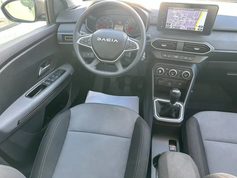 Vue intérieure centrée sur le volant DACIA et la console centrale avec écran tactile et levier de vitesses manuel.