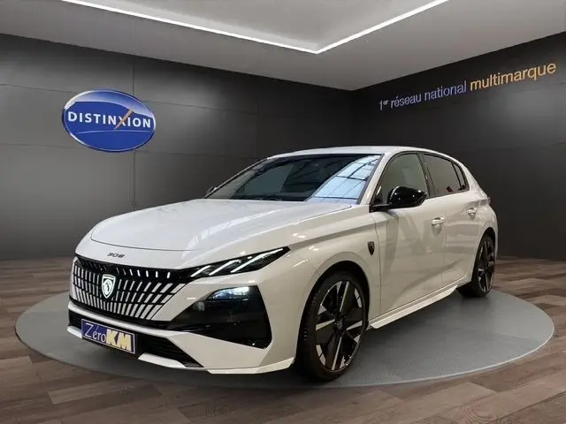 Vue 3/4 avant droite d'une Peugeot 308 Hybrid 145 GT blanche avec calandre distinctive et jantes noires en showroom.