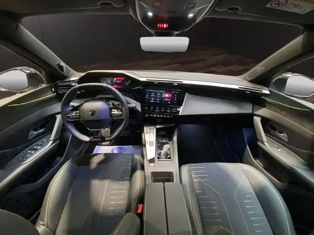 Vue intérieure avant de la Peugeot 308 Hybrid 145 e-DCS6 GT 2026, tableau de bord moderne avec écran tactile central et volant cuir.