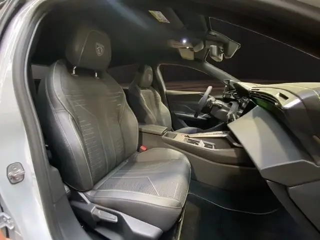 Vue intérieure côté gauche de la Peugeot 308 Hybrid 145 e-DCS6 GT blanche, sièges cuir noirs et tableau de bord moderne.
