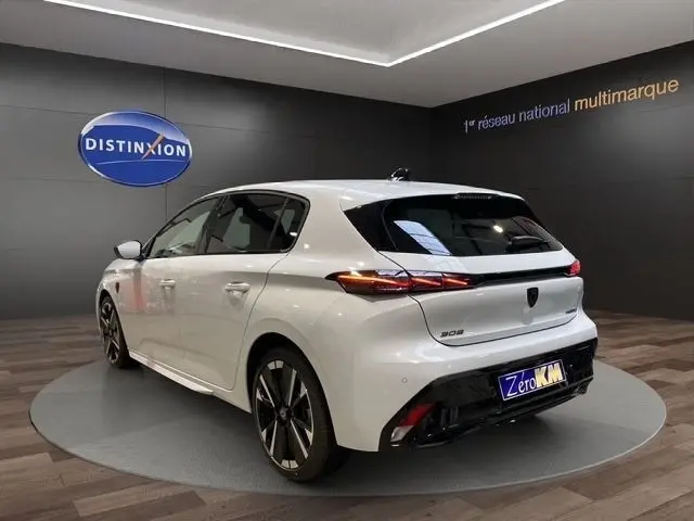 Vue 3/4 arrière gauche d'une Peugeot 308 Hybrid 145 e-DCS6 GT blanche, avec feux arrière LED et jantes alliage distinctives.