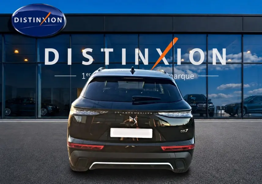 Vue arrière d'un DS7 noir 2026 avec feux LED fins et double sortie d'échappement, devant une vitrine Distinxion.
