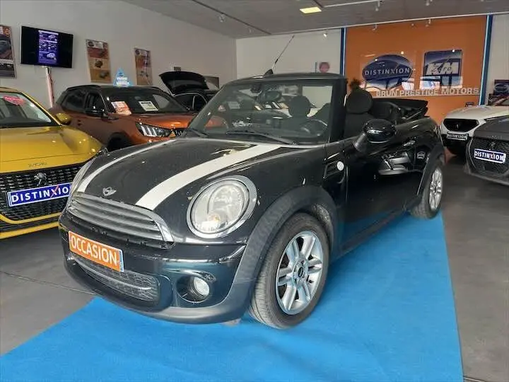 Mini Cooper cabriolet noire vue 3/4 avant droit avec bandes blanches, capote ouverte en concession.