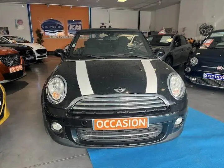Vue avant d'une MINI Cooper cabriolet noire avec bandes blanches sur le capot, en showroom avec panneau "OCCASION" visible.