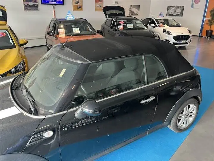 MINI Cooper cabriolet noire vue de trois quarts avant droit avec capote fermée en showroom.